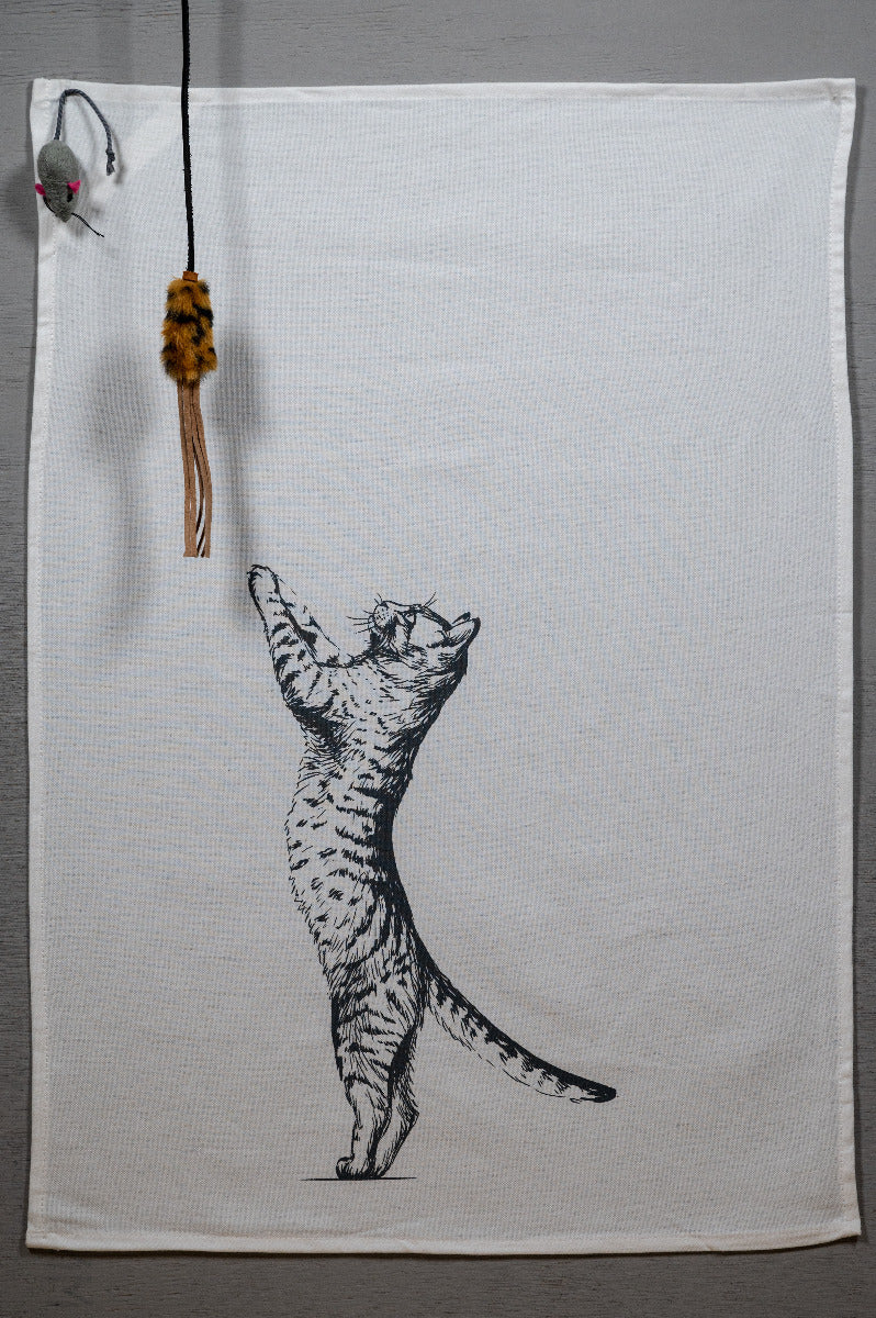 Weißes Geschirrtuch ausgebreitet mit der Katze, die sich nach oben streckt. Und oben links ist eine kleine Maus platziert.