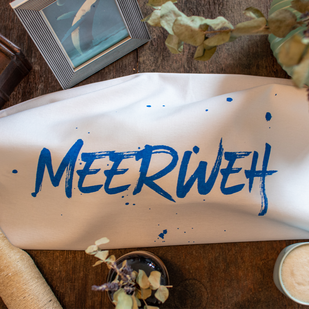 Weißes Geschirrtuch mit der blauen Schrift "Meerweh" hat ein Brot eingerollt