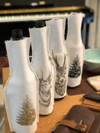 Vier verschiedene weiße Flaschenhussen mit braunem Tannen-Motiv, schwarzen Tannen-Motiv und zwei Hirsch Motiven