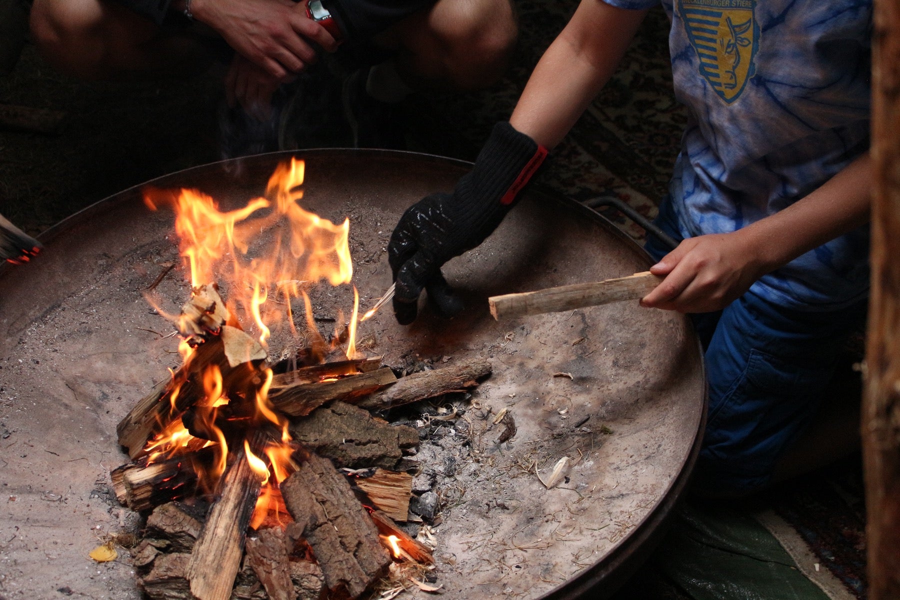 Die Grillhandschuhe im Einsatz, Handschuh hält einen brennenden Holz Spahn über einer Feuerschale