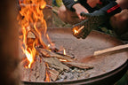 Die Grillhandschuhe im Einsatz, Handschuh hält einen brennenden Holz Spahn über einer Feuerschale