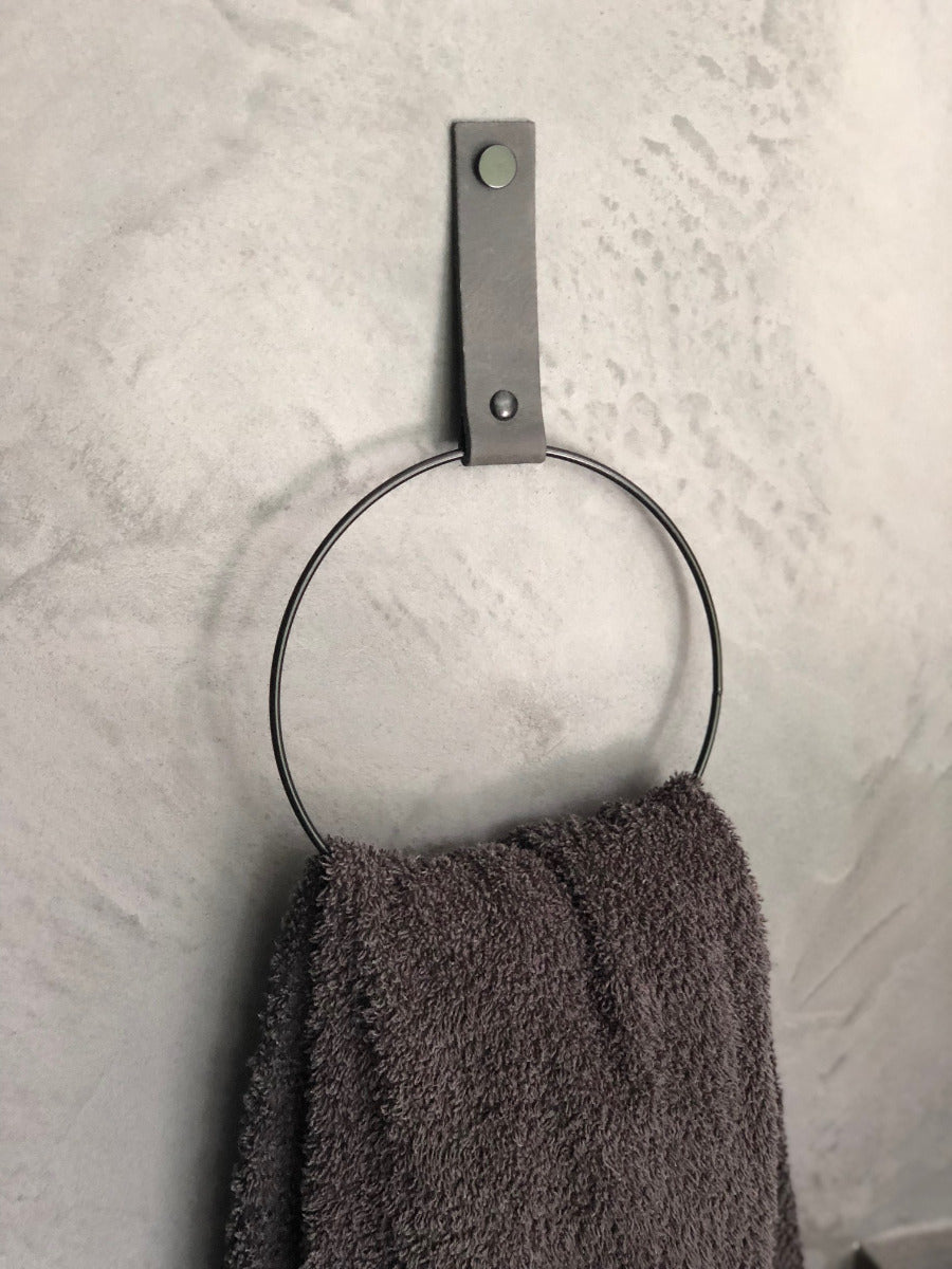 Handtuchhalter in schwarzer Ring Form an der Wand befestigt mit einem dunkel grauen Lederriemen in dessen Ring ein Handtuch hängt