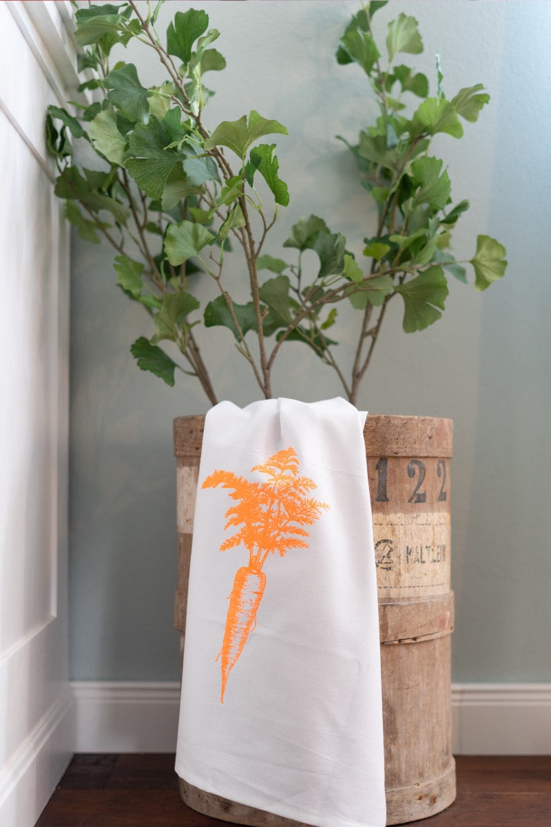 Weißes Geschirrtuch mit einem orangenen Audruck einer Karotte aufgahanden in einem Kübel in dem ein Baum wächst