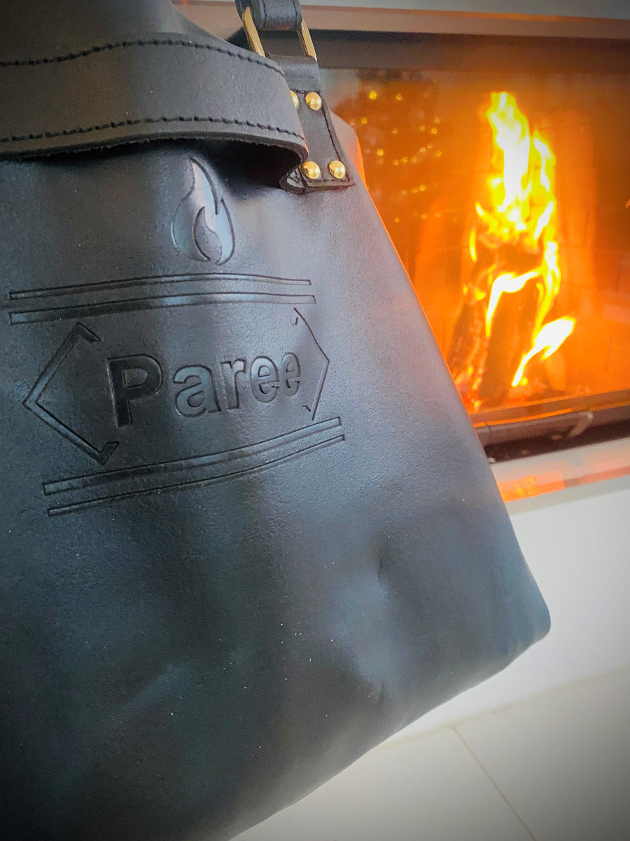 Näheres Bild von dem Brennholzträger aus Leder mit Kamin im Hintergrund, Das Logo von dem Hersteller Paree ist zu sehen