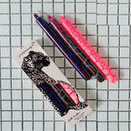 Drei Stabkerzen in Pink, Blau, Hellblau mit einem Trockenriss Muster und eingepackte auf einem Fliesenteppich