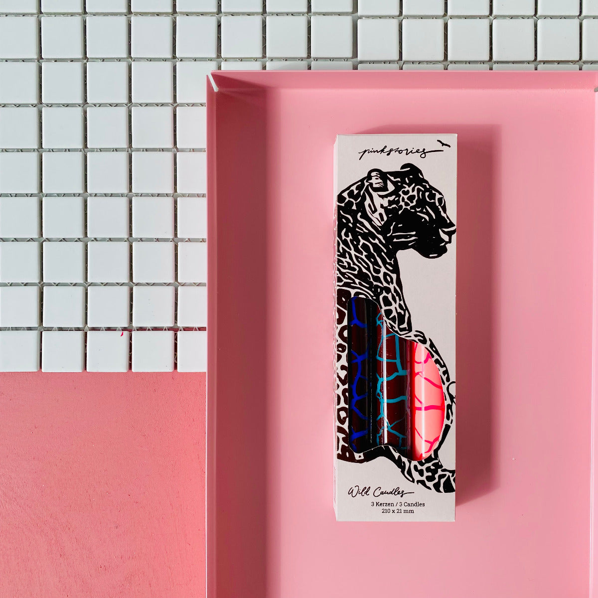 Drei Stabkerzen in Pink, Blau, Hellblau mit einem Trockenriss Muster eingepackt auf einem Pinken HIntergrund