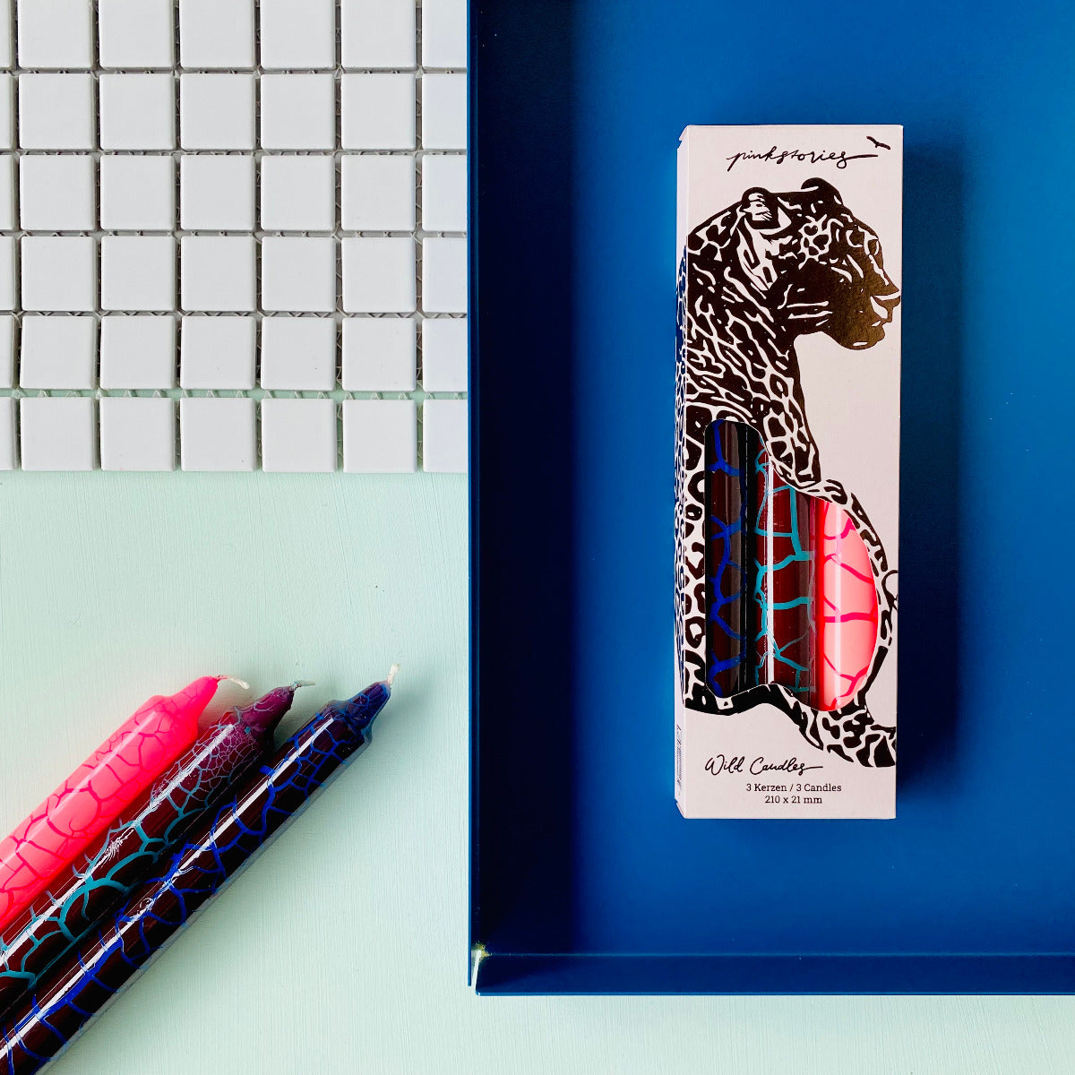 Drei Stabkerzen in Pink, Blau, Hellblau mit einem Trockenriss Muster mit eingepackten Kerzen daneben
