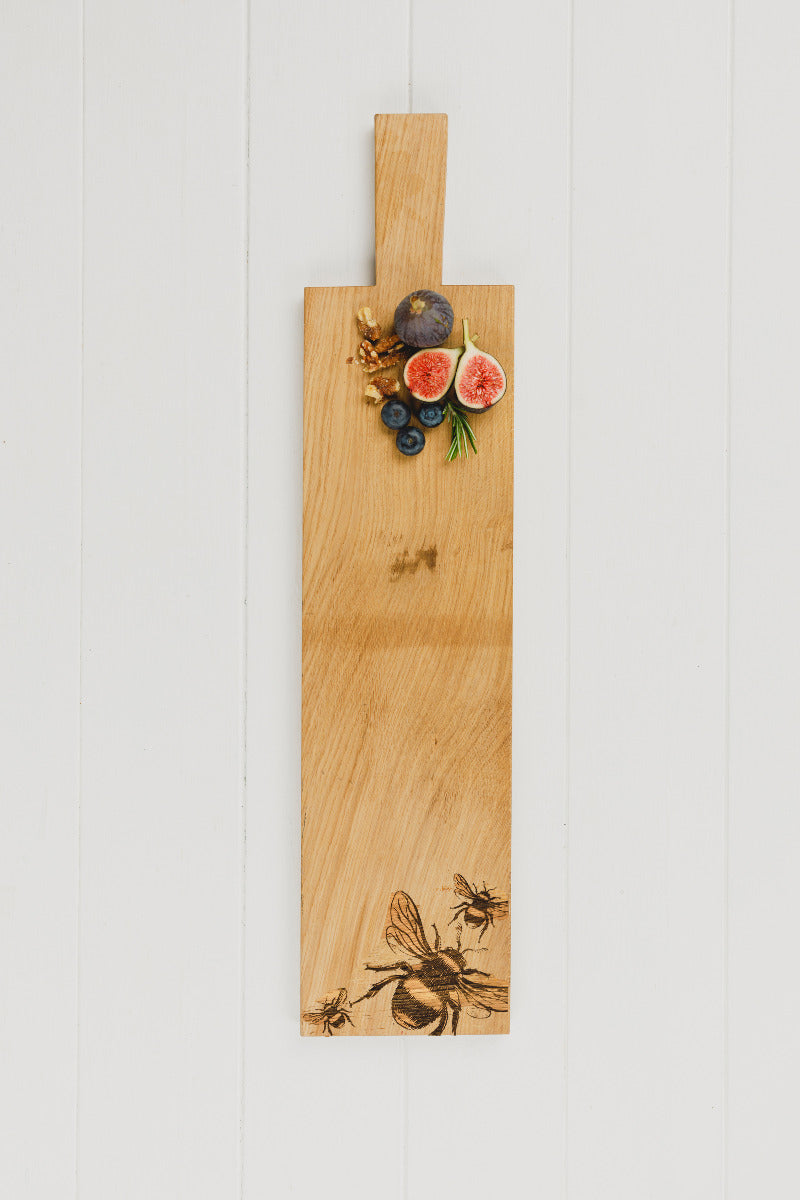 Ein Eichen Servierbrett mit einem eingebrannten Bienen-Design auf dem Deko Früchte liegen