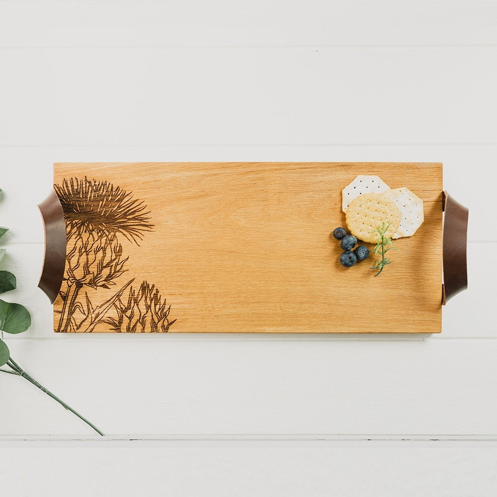 Eichen Serviertablett mit einem eingebrannten Distel Design und zwei braunen Lederriemen, links und rechts um das Tablett zu heben