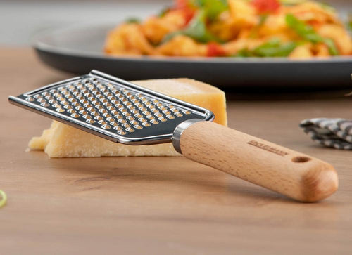 Die Edelstahl Hand Käsereibe mit Holzgriff von Fackelmann liegt auf einem Stück Käse