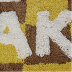 Badvorleger/ Badematte kariert in Braun und Gelb mit der weißen Schrift "Get naked", nahaufnahme der weißen Schrift