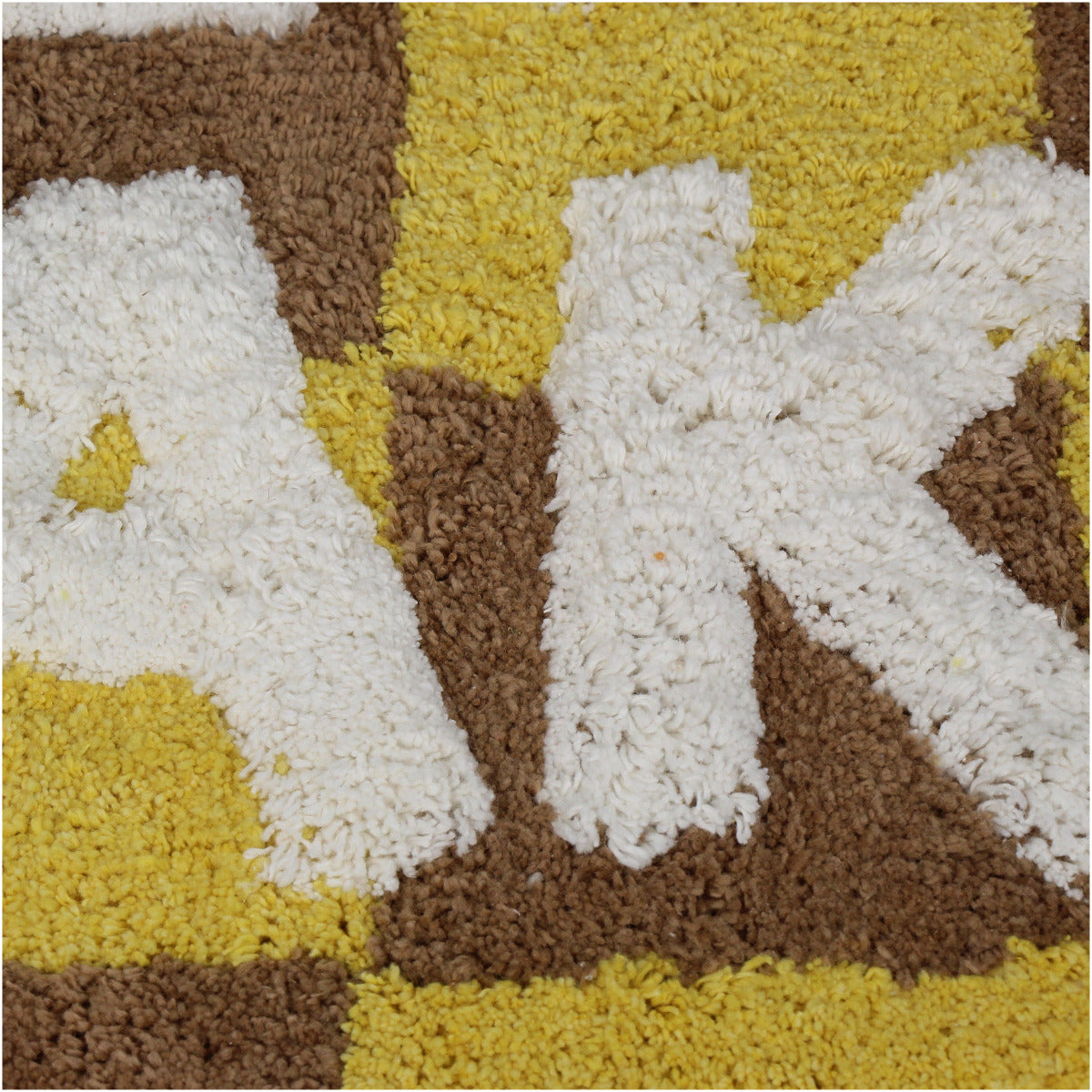 Badvorleger/ Badematte kariert in Braun und Gelb mit der weißen Schrift "Get naked", nahaufnahme der weißen Schrift