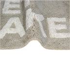 Taupe Badematte mit der weißen Schrift "Get Naked" Nahaufnahme eines teils gebogenen Badvorlegers