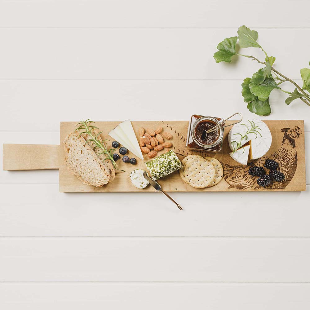 Ein Eichen Servierbrett mit einem eingebranntem "Fasan" Design auf einem Tisch. Sevierbrett angerichtet als edle Antipastiplatte oder als inspiratio für ein Charcuterie Board mit Käse, Brot, usw.
