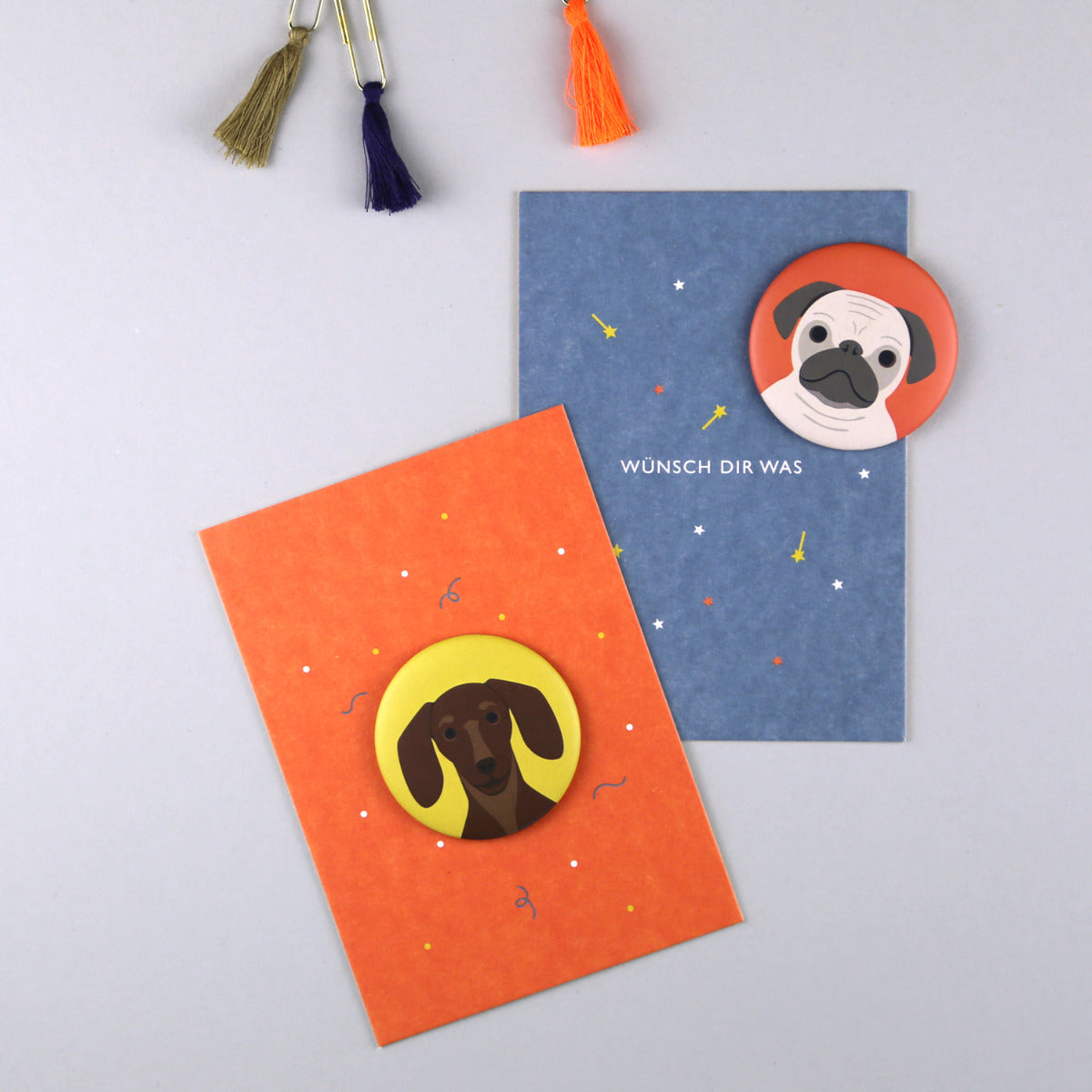 Orangene Postkarte mit Schrift "Lass dich feiern" mit gelbem Magnet mit Dackel Motiv und blaue Karte mit einem Mops Magneten "Wünsch dir was"
