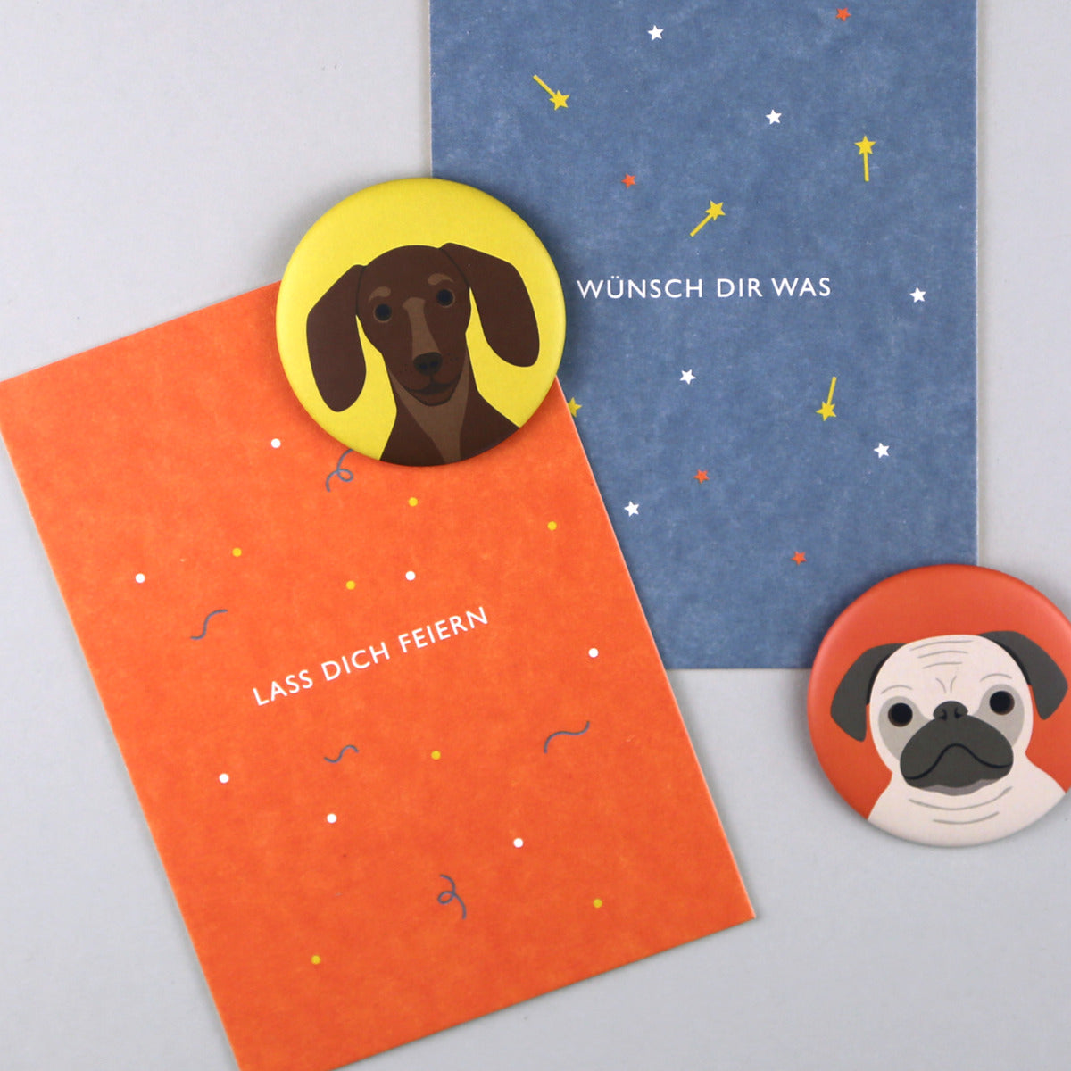 Orangene Postkarte mit Schrift "Lass dich feiern" mit gelbem Magnet mit Dackel Motiv und blaue Karte mit einem Mops Magneten "Wünsch dir was"