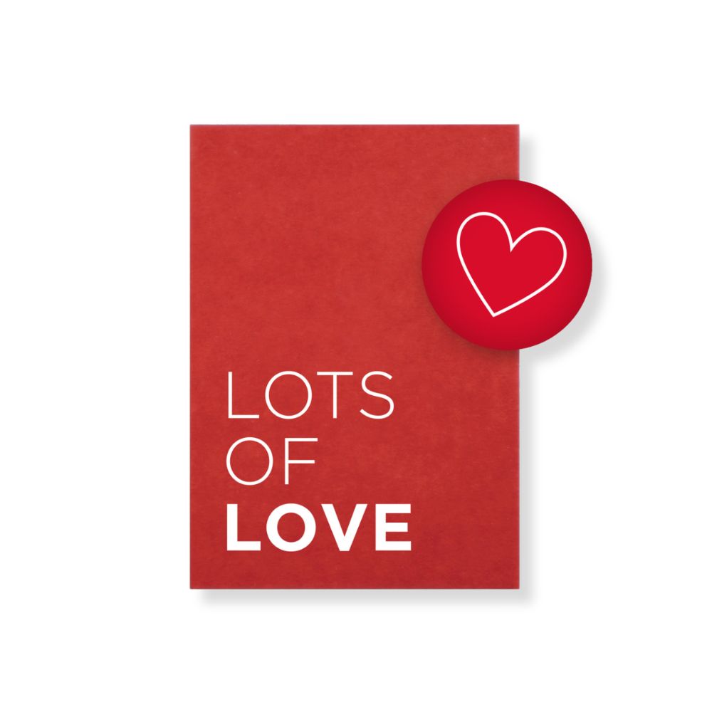 rote Postkarte mit weißer Schrift "Lots of love" und einem roten runden Magnet mit Herz symbol