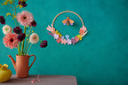 Wanddekoration Wiesenkranz mit einer Biene in der Mitte an einer Wand neben Blumen in einer Vase