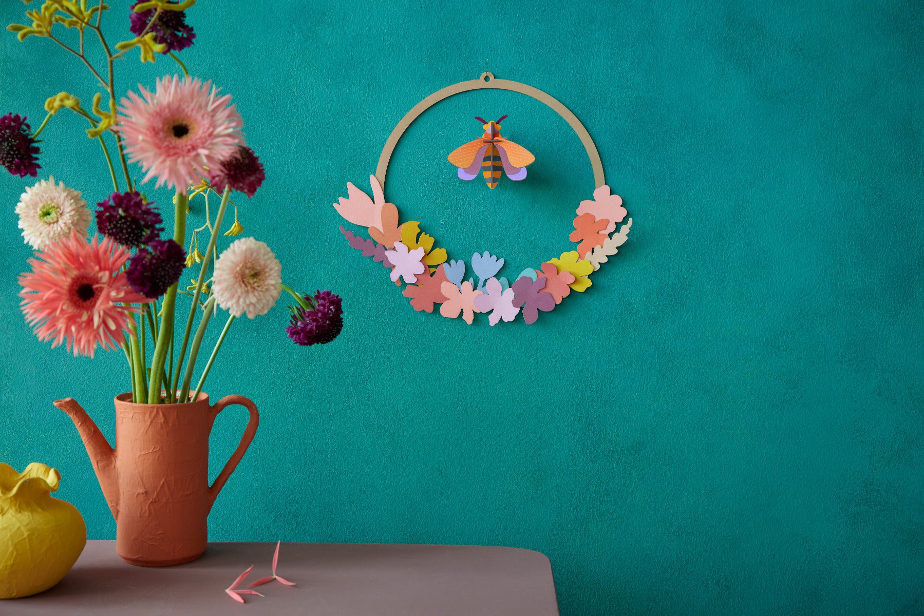 Wanddekoration Wiesenkranz mit einer Biene in der Mitte an einer Wand neben Blumen in einer Vase