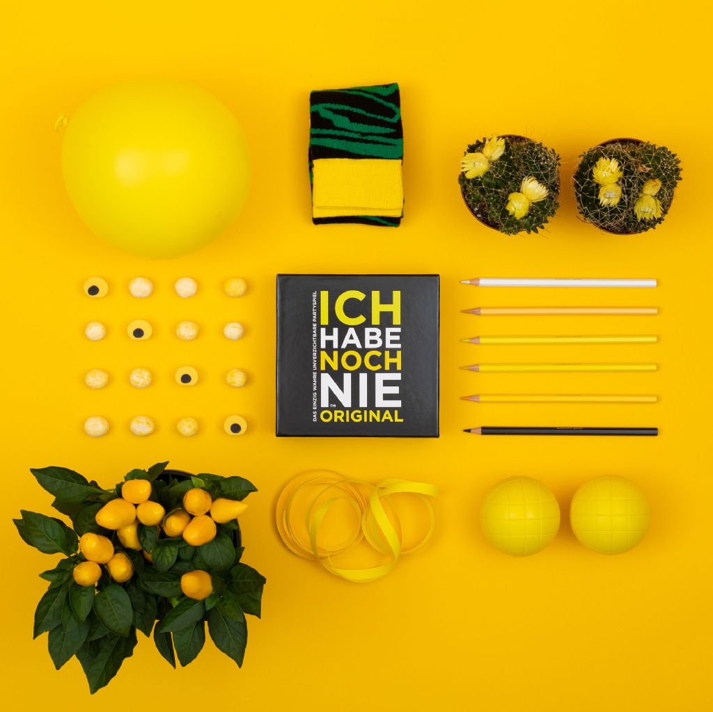 Das Spiel "ICH HABE NOCH NIE" umgeben mit gelbem Dekor, Vogelansicht