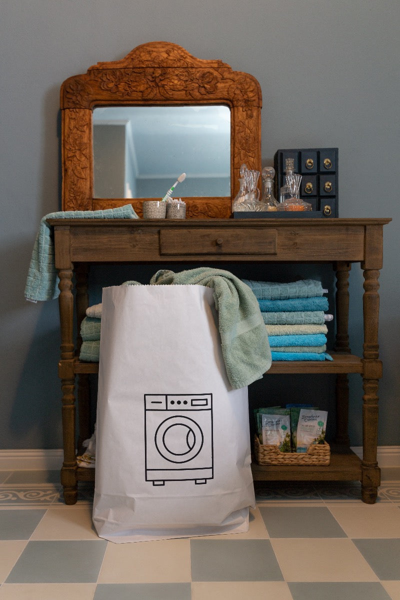 Tüte aus Kraftpapier mit einer aufgedruckten schwarzen Waschmaschine und einem braunen Rand, stehend in einem Badezimmer