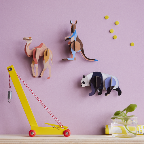 3 Wildtiere 3D Deko Objekte an rosaner Wand angerichtet, Kamel, Känguru und Panda. Im Vordergrund sind Spielzeug eund eine grüne Pflanze dekorativ auf einem Holztisch angerichtet