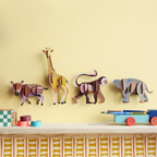 Wildtiere 3D Wanddekoration angerichtet vor einer hellgelben Wand, vier Tiere unter anderem Giraffe, Affe, Elefant, Spielzeuge auf einem Tisch im Vordergrund angerichtet