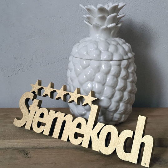 Goldener Holzschriftzug mit der Schrift "Sternekoch" und darüber sind fünf Sterne abgebildet