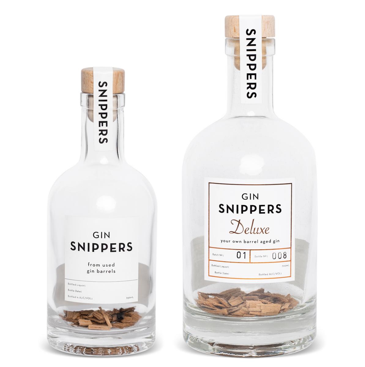 Eine mit Holzschnipsel von alten schottischen Fässern gefüllte, sonst leere GIN-Flasche mit Kork-Verschluss mit der Aufschrift "GIN SNIPPERS Deluxe" und die kleinere Version "GIN SNIPPERS" daneben