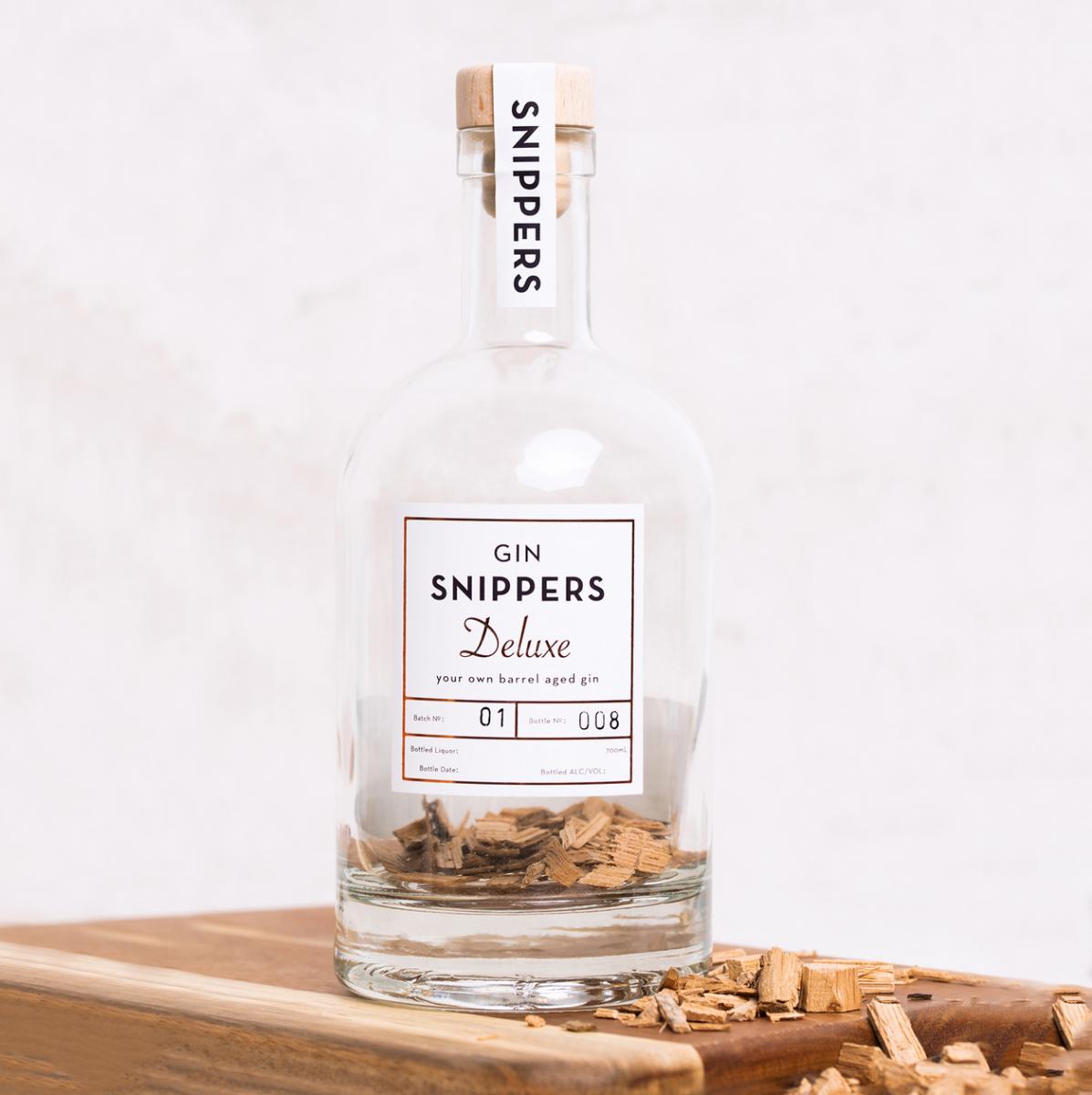 Eine mit Holzschnipsel von alten schottischen Fässern gefüllte, sonst leere GIN-Flasche mit Kork-Verschluss mit der Aufschrift "GIN SNIPPERS Deluxe" mit Nahaufnahme von Label der Flasche