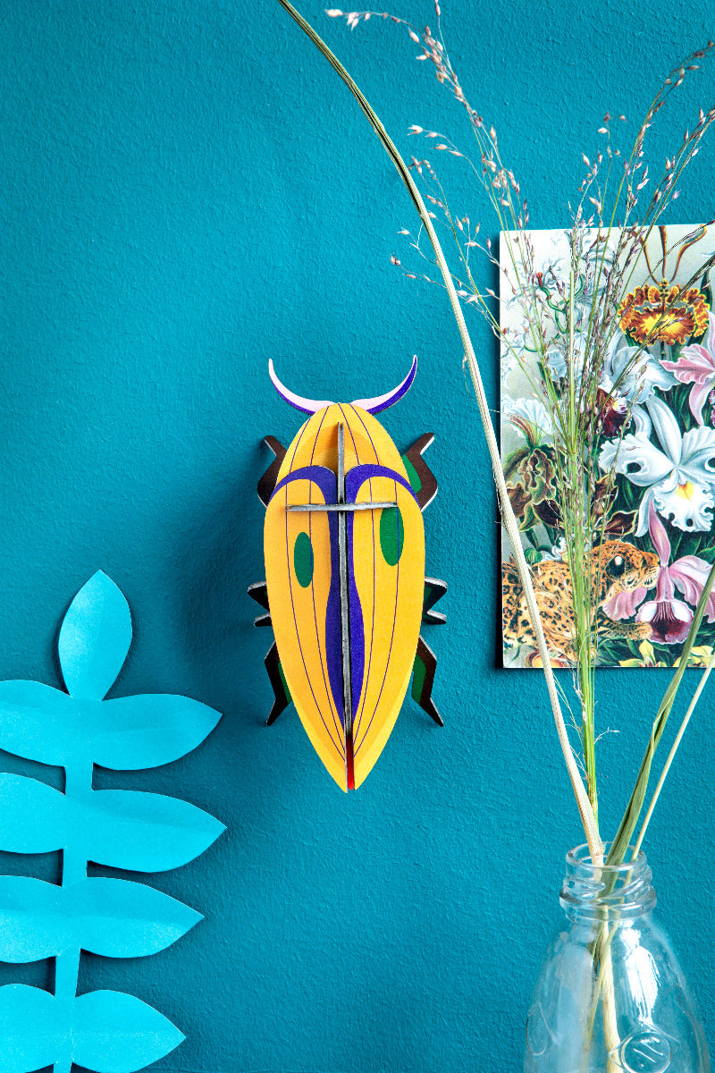 Die Gelbe Käfer Wanddekoration an einer blauen Wand befestigt umgeben von anderen Dekorationsobjekten