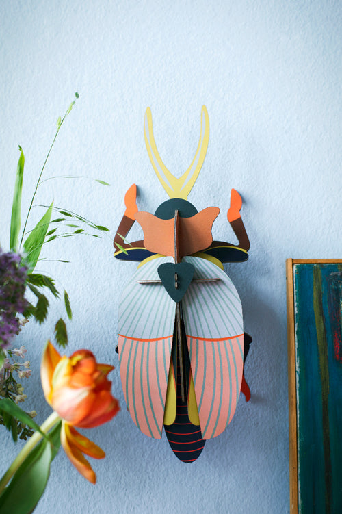3D Wanddekoration eines farbigen Nashorn-Käfers an einer Blauen Wand