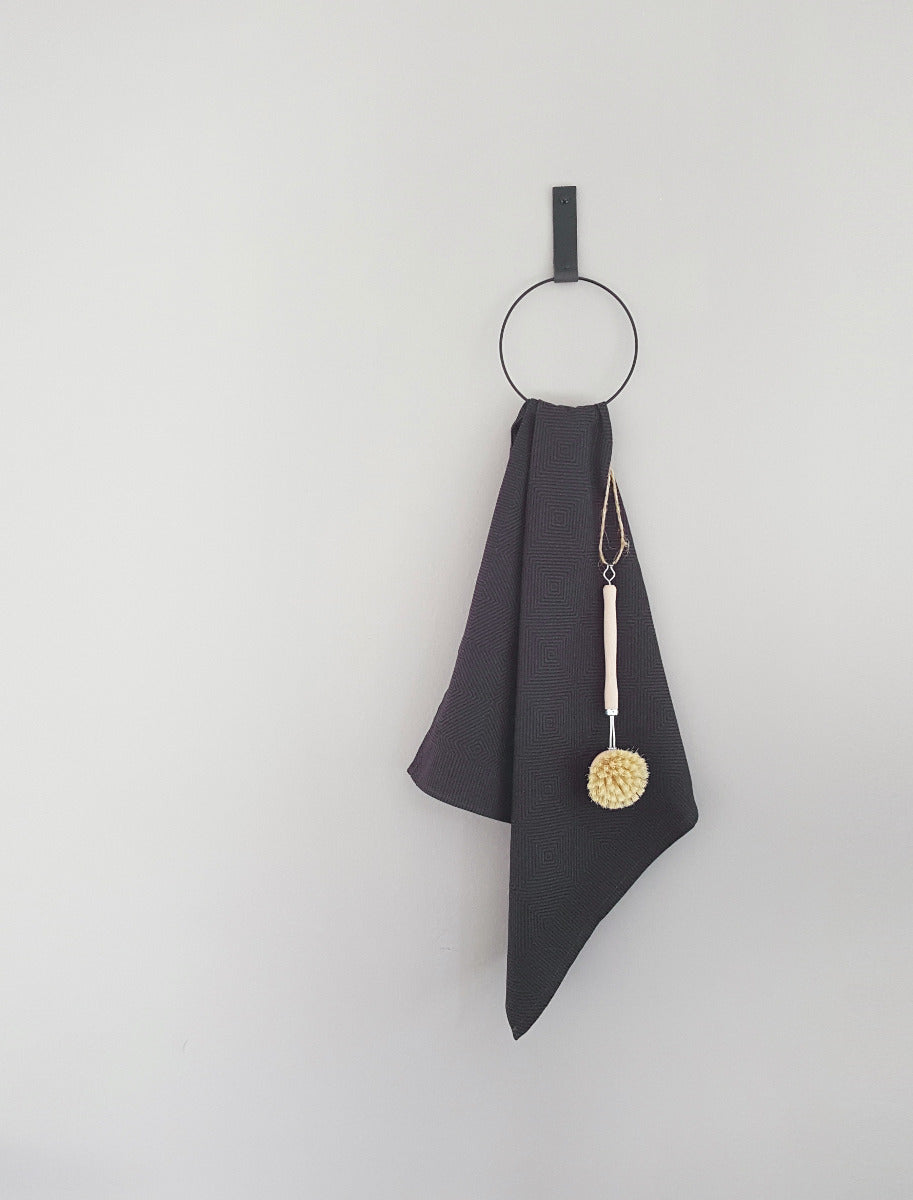 Der Handtuchhalter in Ring Form an der Wand befestigt mit einem schwarzen Lederriemen in dessen Ring ein Handtuch hängt