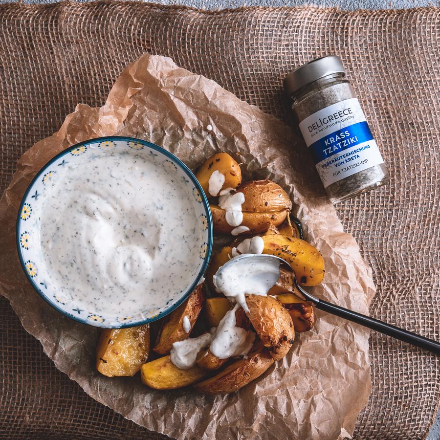 Ein Fläschchen "Krass Tzatziki" Wildkräutermischung von Deligreece neben einer Schüssel Tzatziki gewürzt mit der Mischung und Kartoffelecken