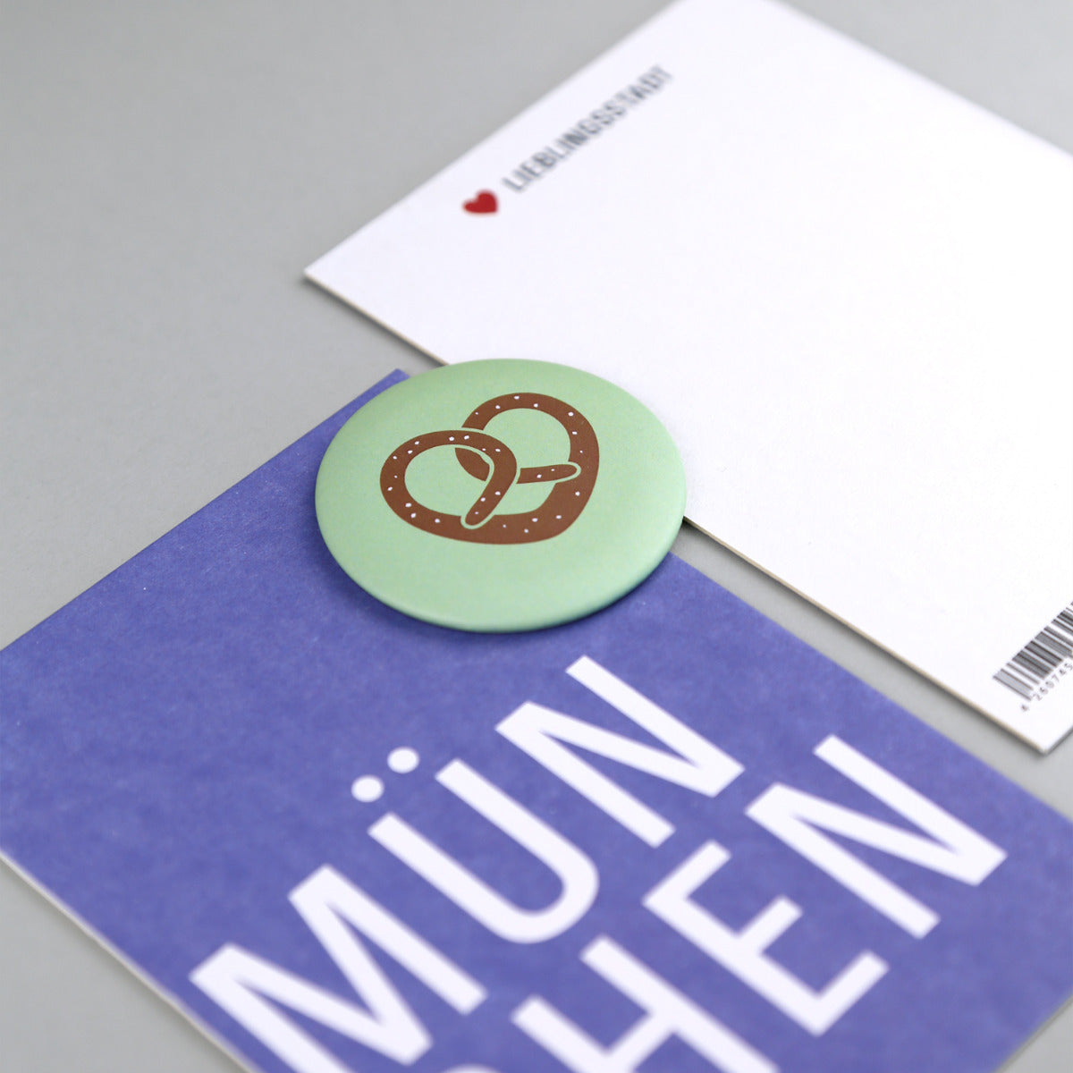 Blaue Postkarte mit Schrift "MÜNCHEN" mit Magnet mit Brezel Motiv mit fokus auf den Magneten