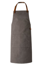 Eine graue Canvas Schürze mit Träger aus braunem Leder.