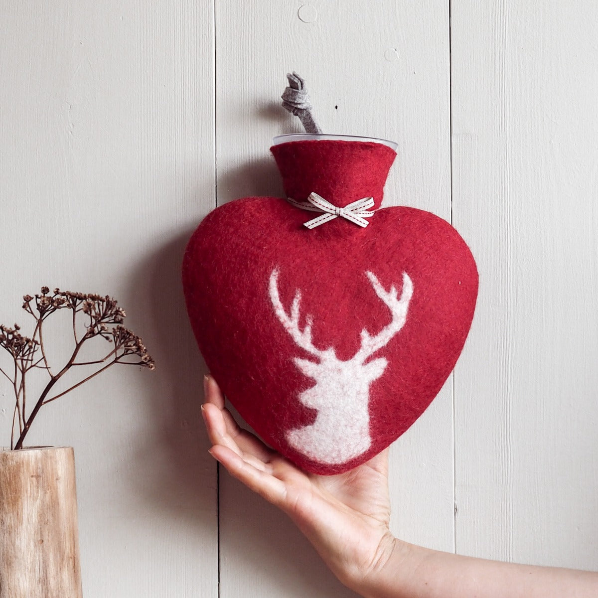 Eine Hand hält die rote Wärmeflasche mit pinkweißem Hirsch Motiv an einer Wand